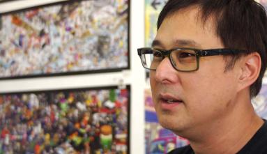 Eric Nakamura in front of a blurred background of colorful framed art